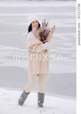 A girl in a beige cardigan and winter flowers walks in nature in the snowy season. Winter weather 97223788