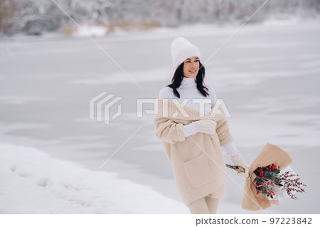 A girl in a beige cardigan and winter flowers walks in nature in the snowy season. Winter weather 97223842