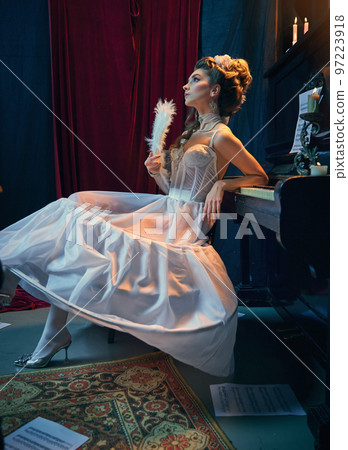Dreams. Portrait of young beautiful girl in image of medieval person, princess in elegant white dress sitting at the piano. Comparison of eras, beauty, history, art 97223918