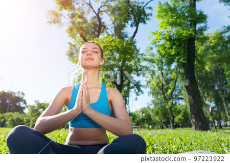 Girl meditates in lotus pose on green grass 97223922