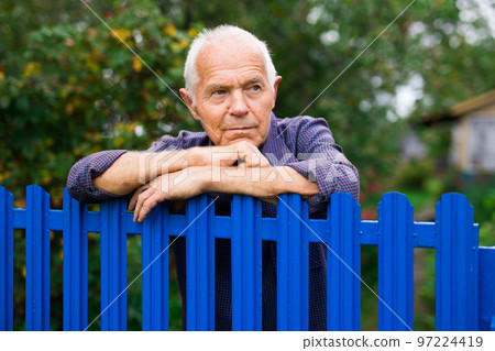 Old man leaning on fence outdoors 97224419