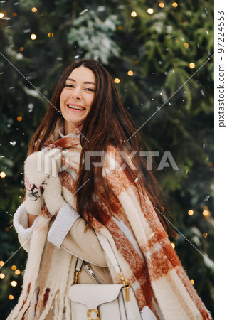 A girl with long hair in a scarf and with a white handbag walks down the street in winter 97224553