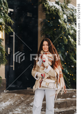 A girl with long hair in a scarf and with a white handbag walks down the street in winter A girl with long hair in a scarf and with a white handbag walks down the street in winter 97224556