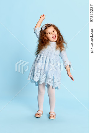 Dance. Studio shot of preschool age girl in blue dress expressing positive emotions isolated over blue background. Happiness, kids fashion concept Dance. Studio shot of preschool age girl in blue dress expressing positive emotions isolated over blue background. Happiness, kids fashion concept 97225227