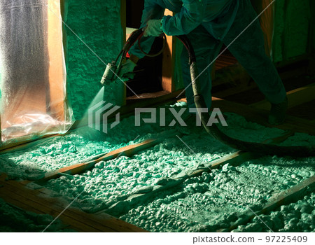 Male builder insulating wooden frame house. Cropped view of man worker spraying polyurethane foam on floor inside of future cottage, using plural component gun. Construction and insulation concept. Male builder insulating wooden frame house. Cropped view of man worker spraying polyurethane foam on floor inside of future cottage, using plural component gun. Construction and insulation concept. 97225409