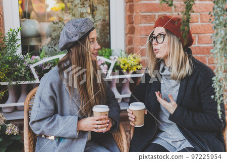Young female best friends talking to each other discussing interesting themes during free time hipster girls joking and having fun together enjoying recreation with coffee to go on urban background Young female best friends talking to each other discussing interesting themes during free time hipster girls joking and having fun together enjoying recreation with coffee to go on urban background 97225954