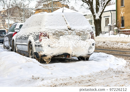 Riga, Latvia - 13 December, 2022: Frozen car covered with snow layer in winter day parked on the street of city. Riga, Latvia - 13 December, 2022: Frozen car covered with snow layer in winter day parked on the street of city. 97226212