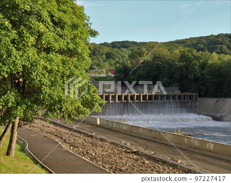 an old dam with a road bridge at the top, standing on the river, visible from the side of the embankment in the city park, a small pressure of water flowing through the locks, control of throughput an old dam with a road bridge at the top, standing on the river, visible from the side of the embankment in the city park, a small pressure of water flowing through the locks, control of throughput 97227417