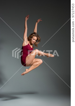 Beautiful woman dancer wearing maroon swimsuit posing on a grey studio background 97227453