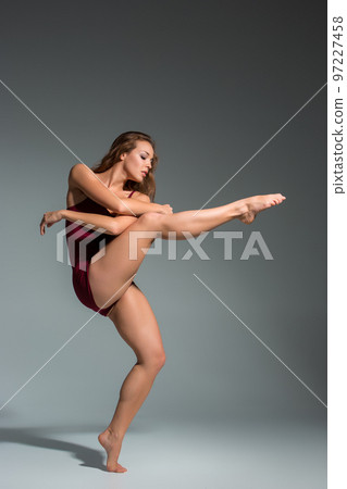 Beautiful woman dancer wearing maroon swimsuit posing on a grey studio background 97227458