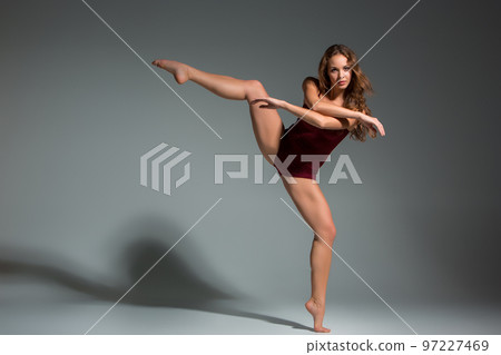 Beautiful woman dancer wearing maroon swimsuit posing on a grey studio background Beautiful woman dancer wearing maroon swimsuit posing on a grey studio background 97227469