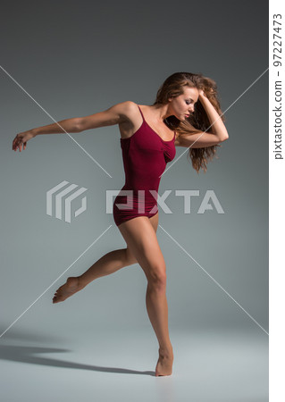Beautiful woman dancer wearing maroon swimsuit posing on a grey studio background Beautiful woman dancer wearing maroon swimsuit posing on a grey studio background 97227473
