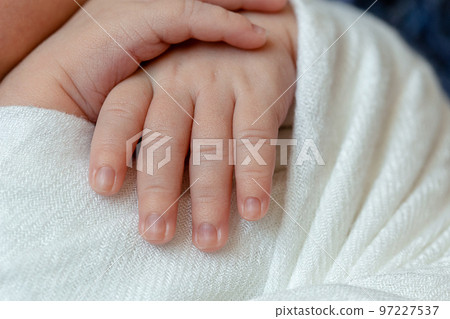Close-up of little baby handles. The sleeping Newborn boy under a white knitted blanket lies on the blue fur. Close-up of little baby handles. The sleeping Newborn boy under a white knitted blanket lies on the blue fur. 97227537