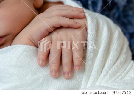Close-up of little baby handles. The sleeping Newborn boy under a white knitted blanket lies on the blue fur. 97227540