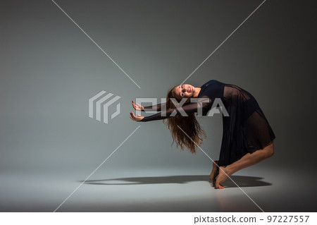 Young beautiful dancer in black dress posing on a dark gray studio background 97227557