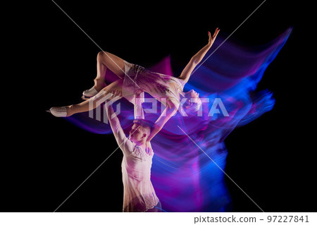 Portrait of young man and woman, figure skating athletes dancing isolated over black background in neon with mixed lights. Support 97227841