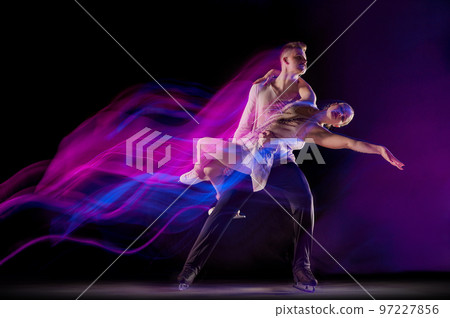 Portrait of young man and woman, figure skating athletes dancing isolated over black background in neon with mixed lights 97227856