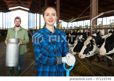 Portrait of female farmer with shovel standing in cowshed 97228546