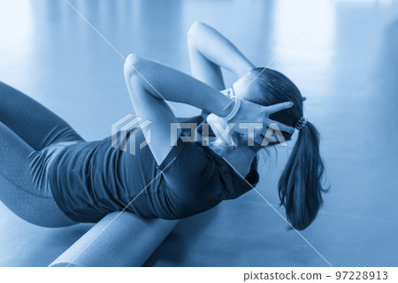 Attractive female doing foam roller exercise relaxing her back and posing in modern bright fitness center 97228913