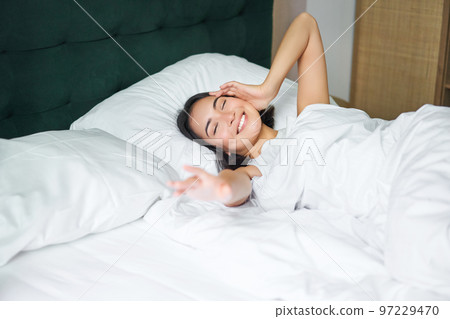 Romantic asian girl waking up in cozy bedroom, lying in bed with white sheets, stretching her hand towards empty pillow Romantic asian girl waking up in cozy bedroom, lying in bed with white sheets, stretching her hand towards empty pillow 97229470