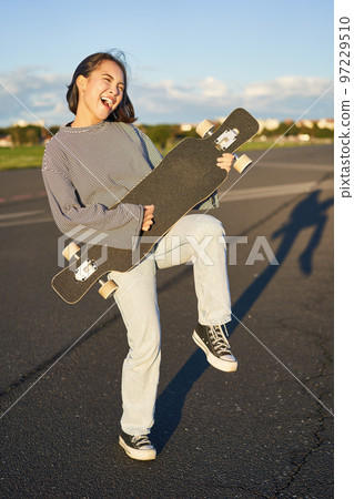 Funny asian girl enjoying skating, holding skateboard like guitar and shadow playing, having fun outdoors Funny asian girl enjoying skating, holding skateboard like guitar and shadow playing, having fun outdoors 97229510