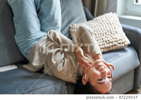 Happy beautiful girl listening music, lying on sofa and relaxing, enjoying stay at home 97229537