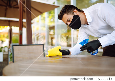 Disinfecting to prevent COVID-19. Waiter cleaning the table with Disinfectant Spray in a restaurant. Disinfecting to prevent COVID-19. Waiter cleaning the table with Disinfectant Spray in a restaurant. 97229713