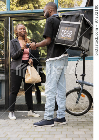 Office worker paying for food delivery with credit card, pos terminal contactless payment for order. African american courier with backpack delivering restaurant meal to customer outdoors Office worker paying for food delivery with credit card, pos terminal contactless payment for order. African american courier with backpack delivering restaurant meal to customer outdoors 97232180