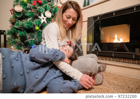 Mother and daughter hugging and smiling, winter evening together at home in a decorated living room 97232200