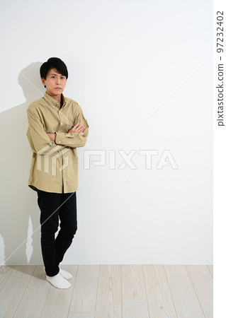 Young man standing against white wall Young man standing against white wall 97232402