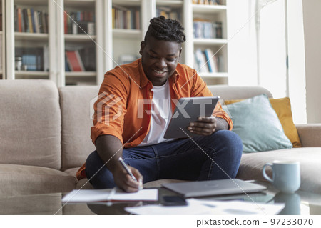 Black businessman sitting at home, looking at screen of tablet Black businessman sitting at home, looking at screen of tablet 97233070