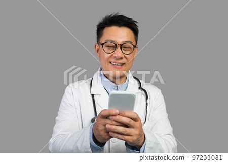 Cheerful adult japanese male therapist in white coat and glasses with stethoscope typing on phone 97233081