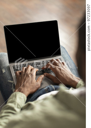 Mature black guy typing on computer keyboard with blank screen, recommends website in living room Mature black guy typing on computer keyboard with blank screen, recommends website in living room 97233097