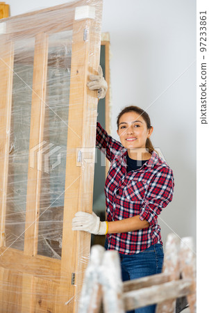 Positive woman carrying wooden door during renovation works 97233861
