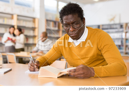 Adult aframerican man reading books and making notes in library Adult aframerican man reading books and making notes in library 97233909