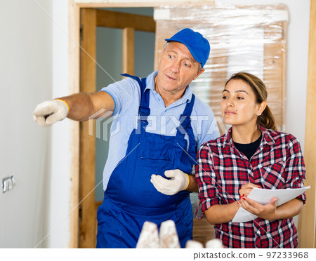 Casual middle-aged repairer in uniform discussing the future construction site with the female in the house 97233968