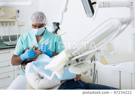 Professional dentist performing teeth treatment to woman in clinic Professional dentist performing teeth treatment to woman in clinic 97234222