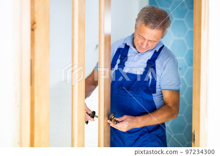 Professional door installer picks up door handles to install on new wooden door Professional door installer picks up door handles to install on new wooden door 97234300