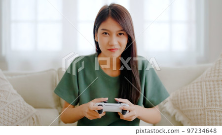 Beautiful young asian woman sitting on sofa and holding joystick playing online video game Beautiful young asian woman sitting on sofa and holding joystick playing online video game 97234648