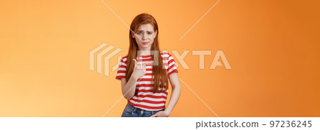 Upset uneasy cute ginger gitl long natural red hair, frowning smirking hesitant, complain, looking suspicious and doubtful point left, not sure if product really good, feel unsure, orange background 97236245