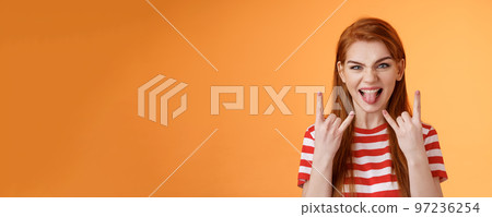 Lets rock-n-roll. Daring cheerful good-looking caucasian redhead woman, having fun, show heavy metal gestures, stick tongue and smile amused, enjoy music festival, stand orange background Lets rock-n-roll. Daring cheerful good-looking caucasian redhead woman, having fun, show heavy metal gestures, stick tongue and smile amused, enjoy music festival, stand orange background 97236254