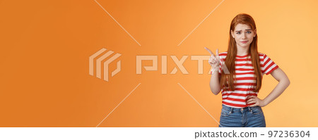 Doubtful redhead girl not buy your talks, smirking hesitant express disbelief, unimpressed about suspicious offer, pointing upper left corner wondered, stand orange background uncertain 97236304