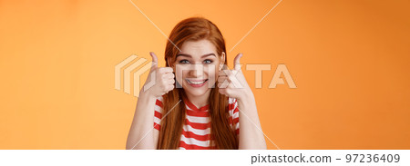 Hopeful cheerful cute redhead girlfriend rooting for you, believe win, smiling supportive satisfied, show thumbs-up delighted, approve choice, wish good luck, encourage friend, orange background 97236409