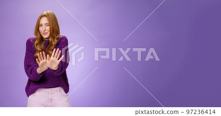 Gross take it away. Portrait of disgusted redhead woman step back and waving palms over body in refusal and no gesture grimacing and squinting from bad smell or aversion over purple wall Gross take it away. Portrait of disgusted redhead woman step back and waving palms over body in refusal and no gesture grimacing and squinting from bad smell or aversion over purple wall 97236414