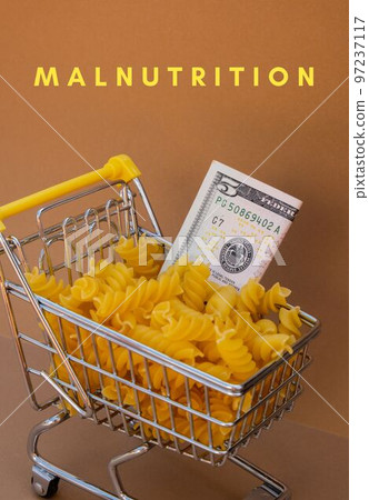 MALNUTRITION text against Shopping trolley cart Filled With Pasta with 5 US dollar paper money banknote on Beige background. Food and groceries shopping price increase, Rising food cost food crisis MALNUTRITION text against Shopping trolley cart Filled With Pasta with 5 US dollar paper money banknote on Beige background. Food and groceries shopping price increase, Rising food cost food crisis 97237117