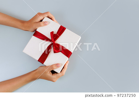 Women's hands hold a white with a red ribbon bow Women's hands hold a white with a red ribbon bow 97237250