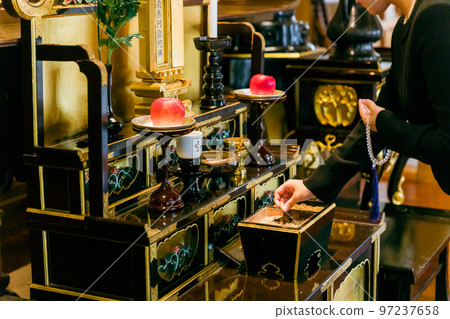 Hands of a woman in mourning clothes standing on an incense stand at a funeral (incense) 97237658