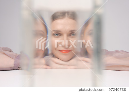 Beautiful woman looking through glass water looks into camera, bright orange Beautiful woman looking through glass water looks into camera, bright orange 97240788