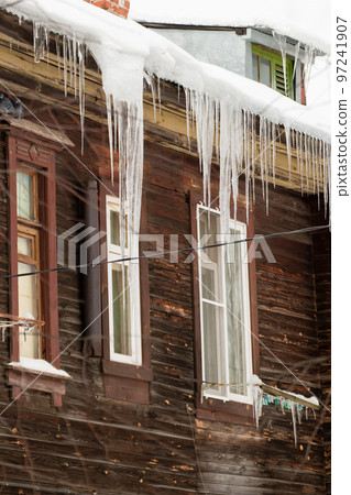 Multiple icicles hang on the edge of the roof, winter or spring.  97241907