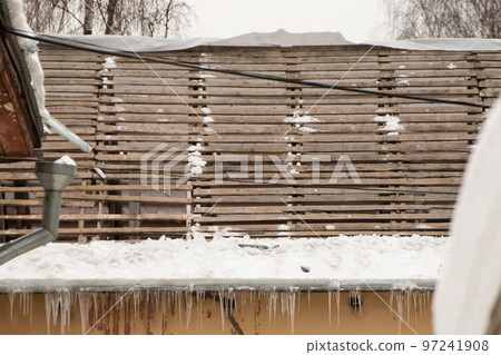 A dismantled roof with a wooden crate and hanging icicles on the edge. A dismantled roof with a wooden crate and hanging icicles on the edge. 97241908